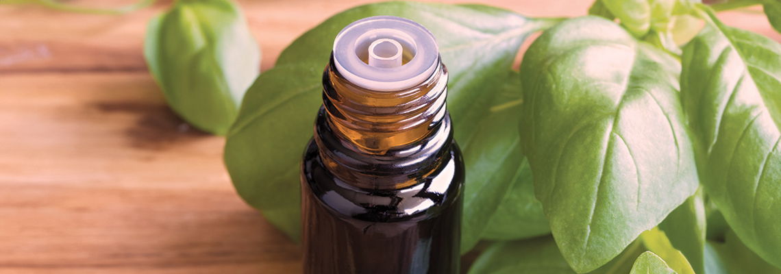 A bottle of essential oil beside fresh basil leaves on a wooden surface.