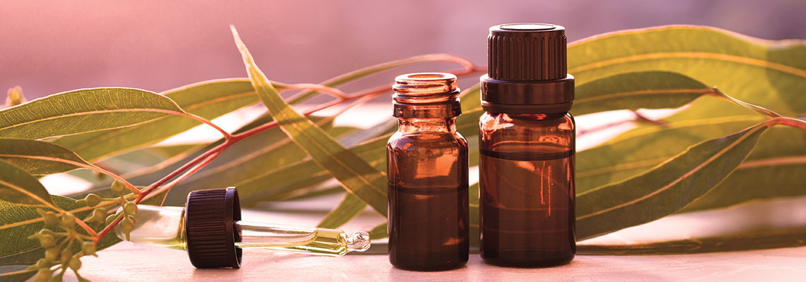 Bottles of essential oils with green leaves in the background.