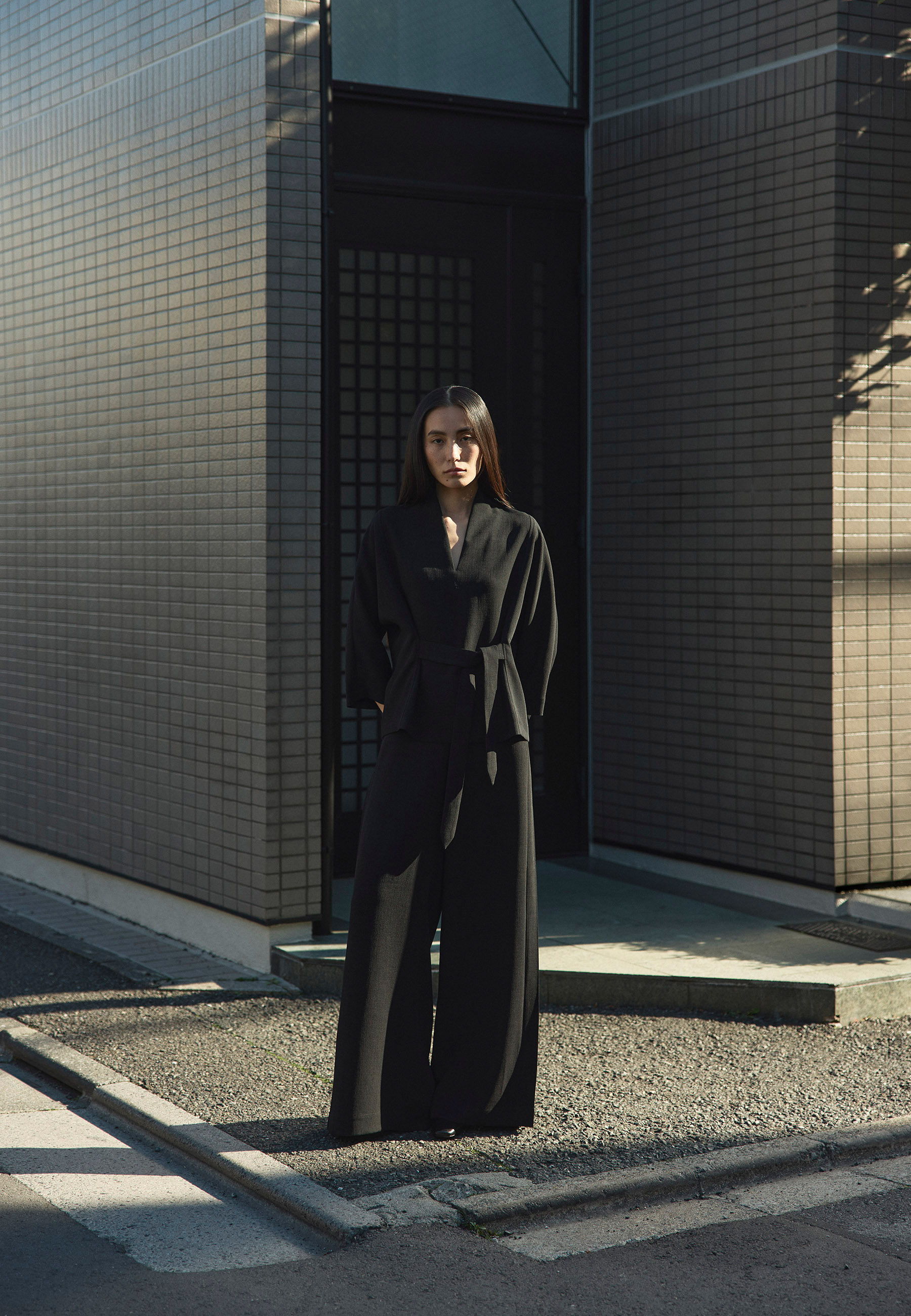 A person in a black outfit standing in front of a modern building.