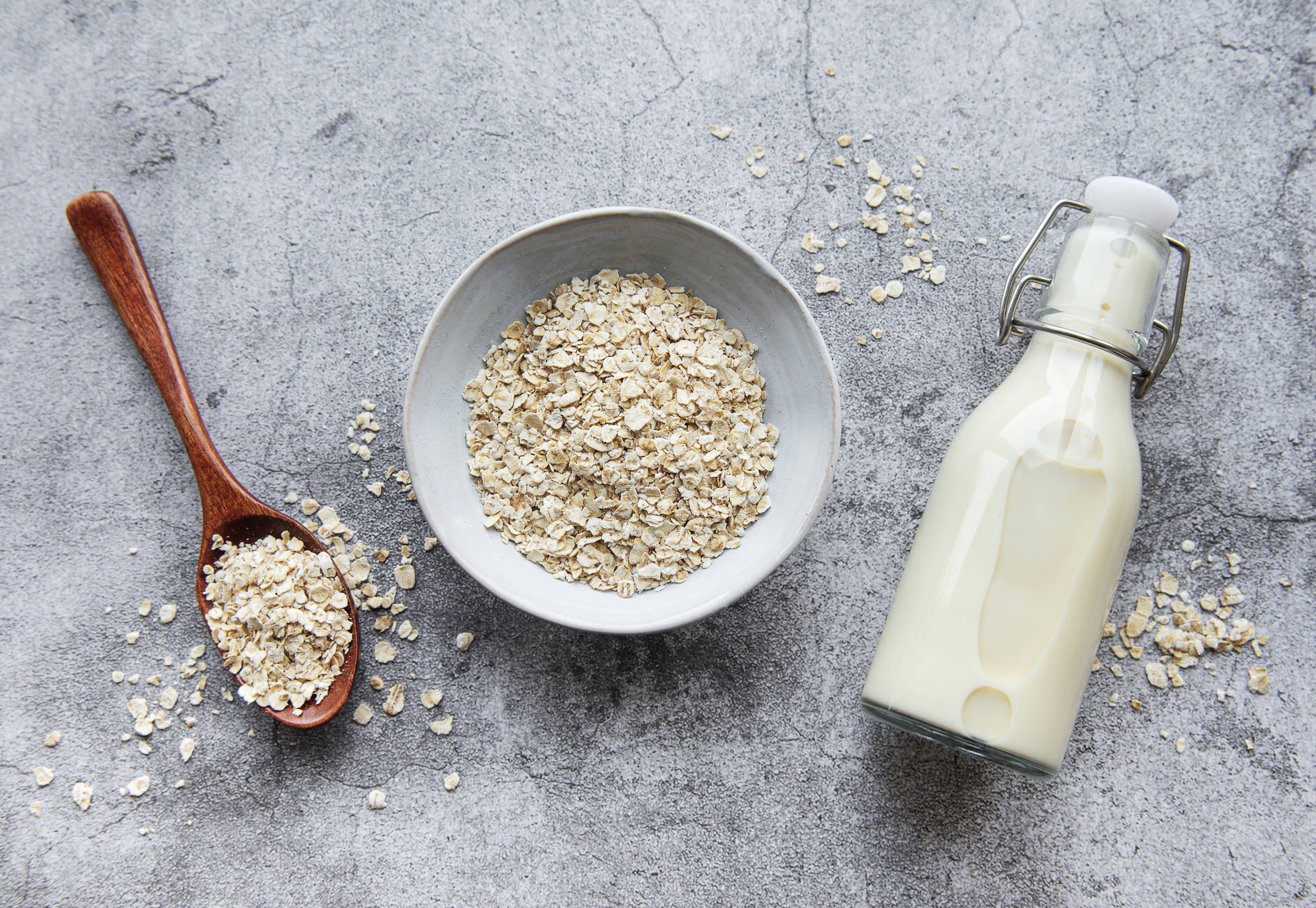 image of the components of an oat vanilla protein shake, rolled oats in a ceramic bowl and milk in a glass bottle, laid on a concrete effect tabletop