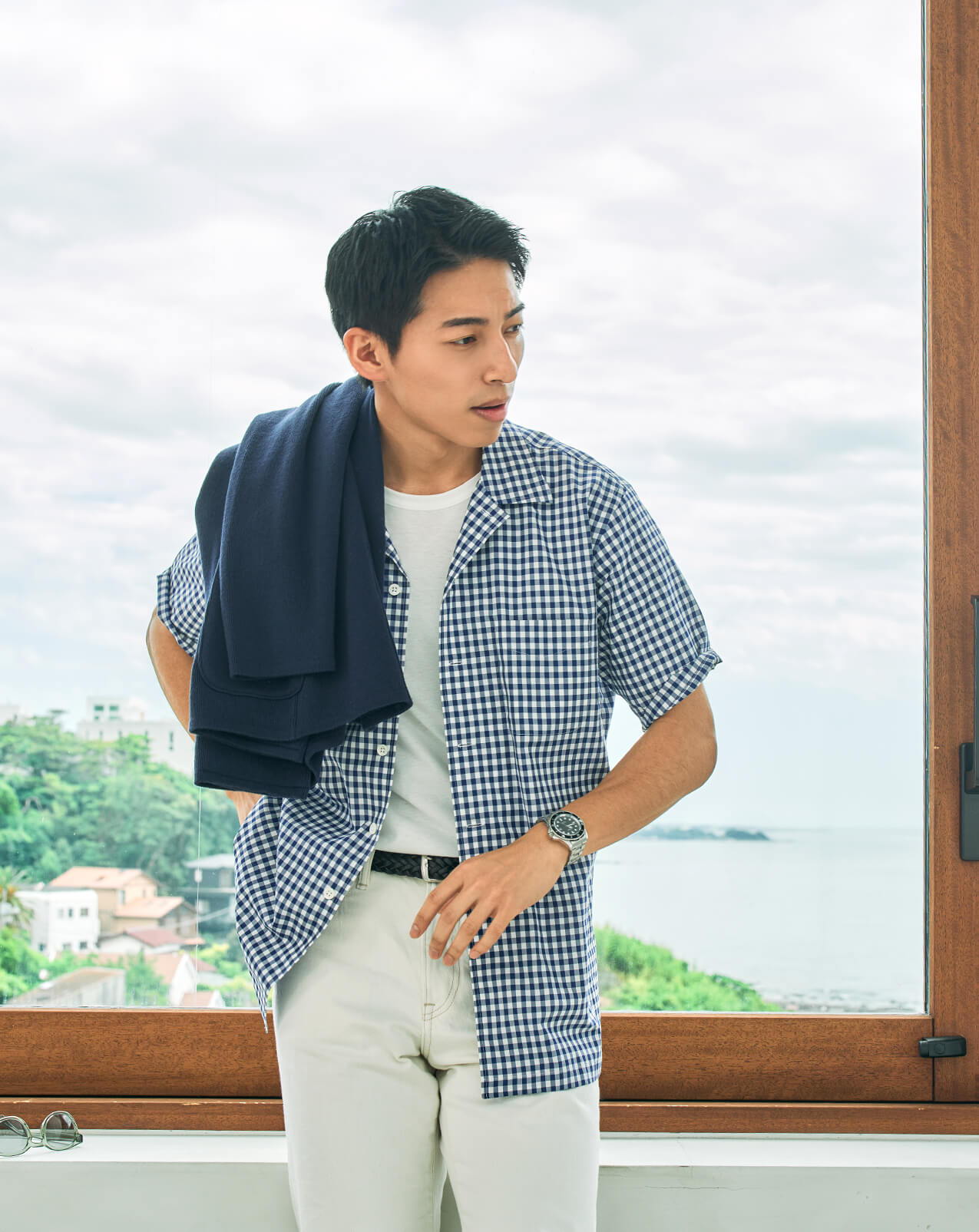 Person wearing a checkered shirt and pants, standing by a window.