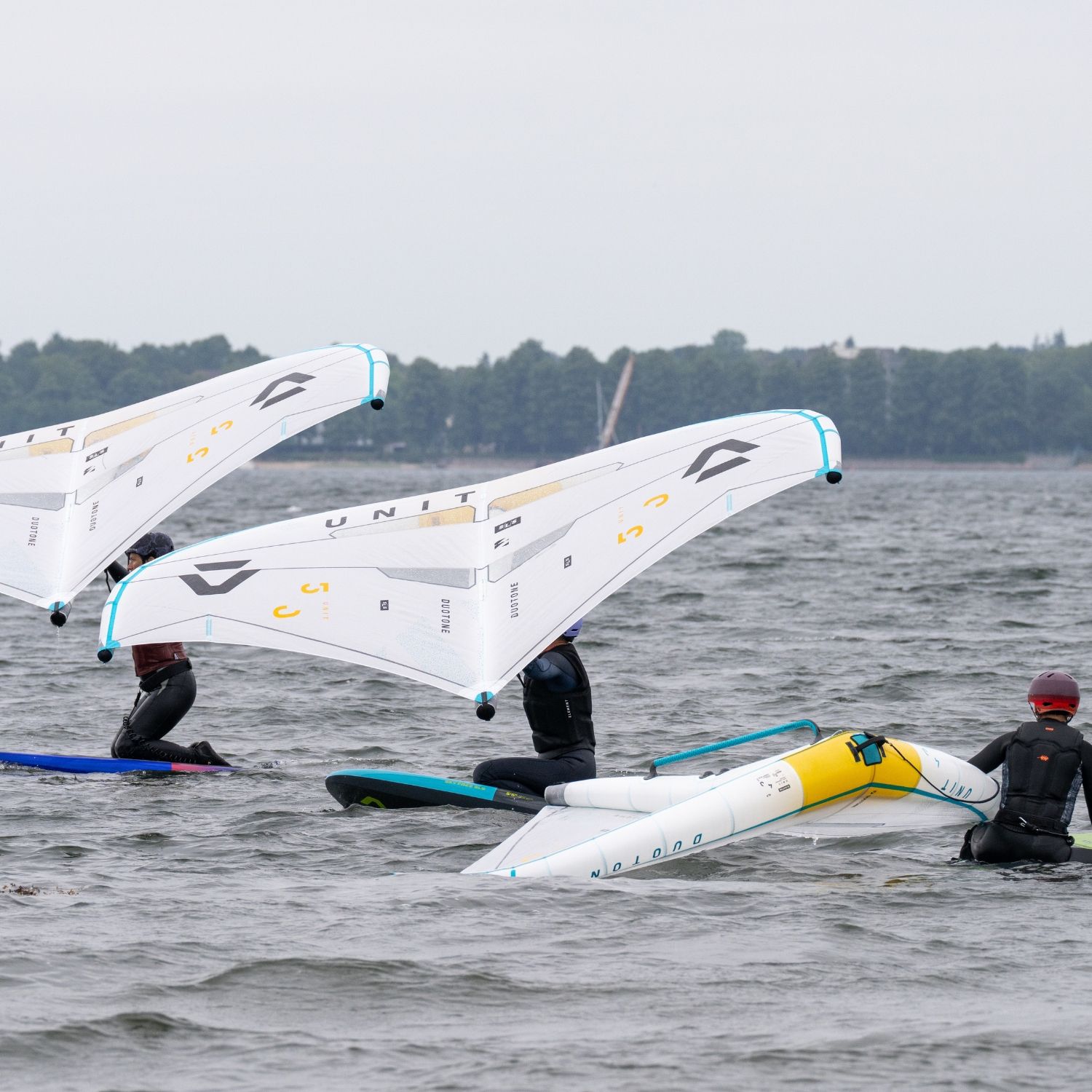 Three surfers on water with wings, one surfer capsized.