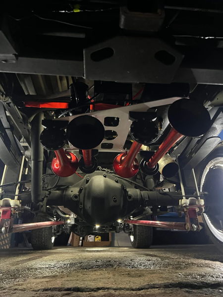 Four red train horns mounted to white plate above differential in indoor garage