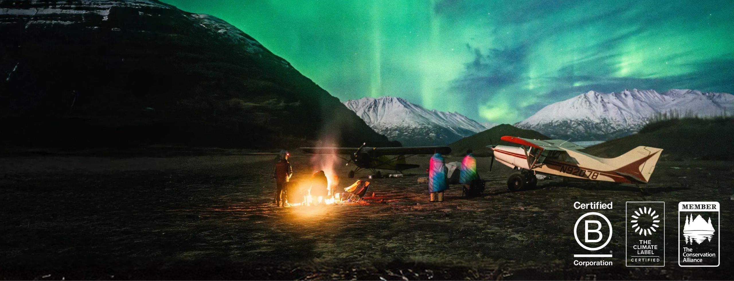 Campfire under the northern lights with mountains in the background.
