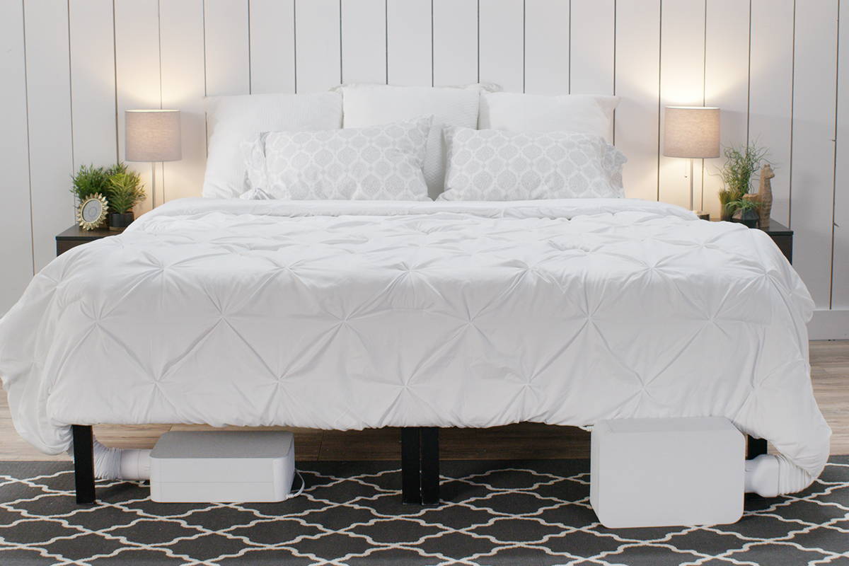 Bed with white bedspread and white pillows, with two BedJet units attached at the foot of the bed, one on each side.