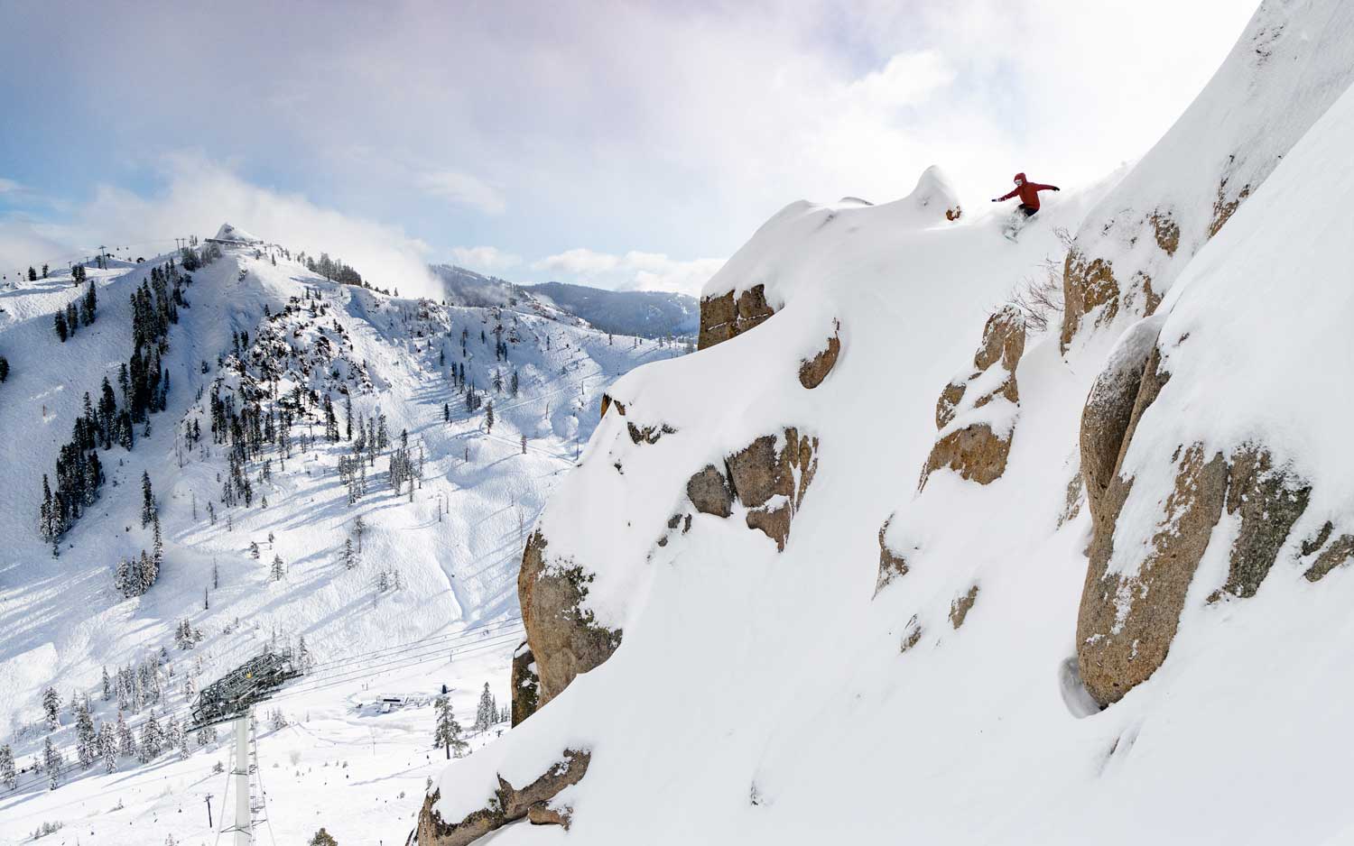 Person snowboarding down a snowy mountain slope with rocky terrain.