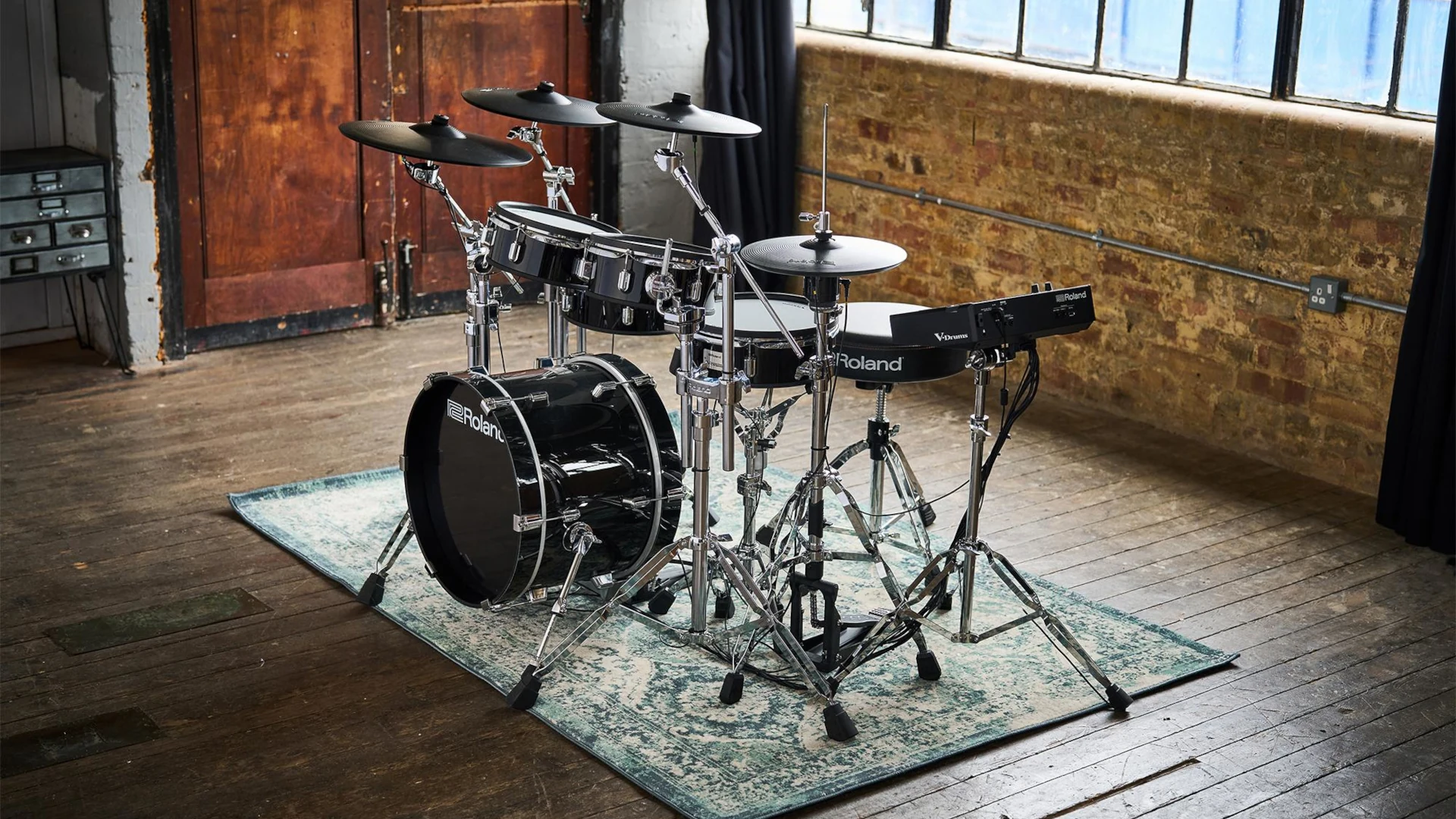 Electronic drum set on a rug in a spacious room with large windows.