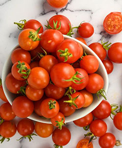 A bowl filled with fresh red cherry tomatoes on a marble surface.