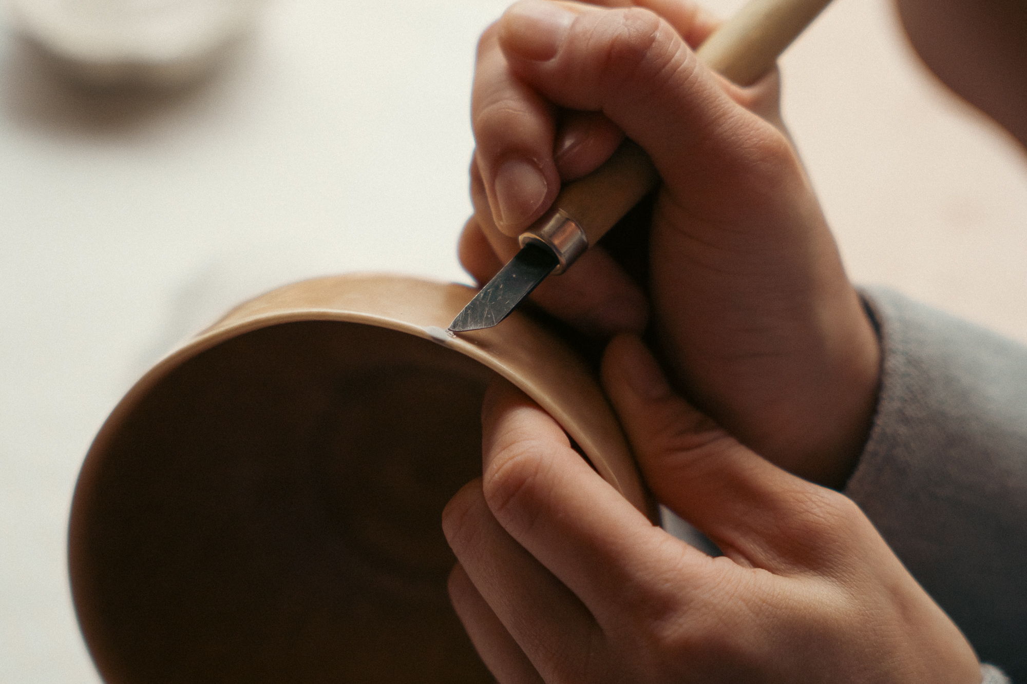 A person carving a design into a clay bowl with a tool.