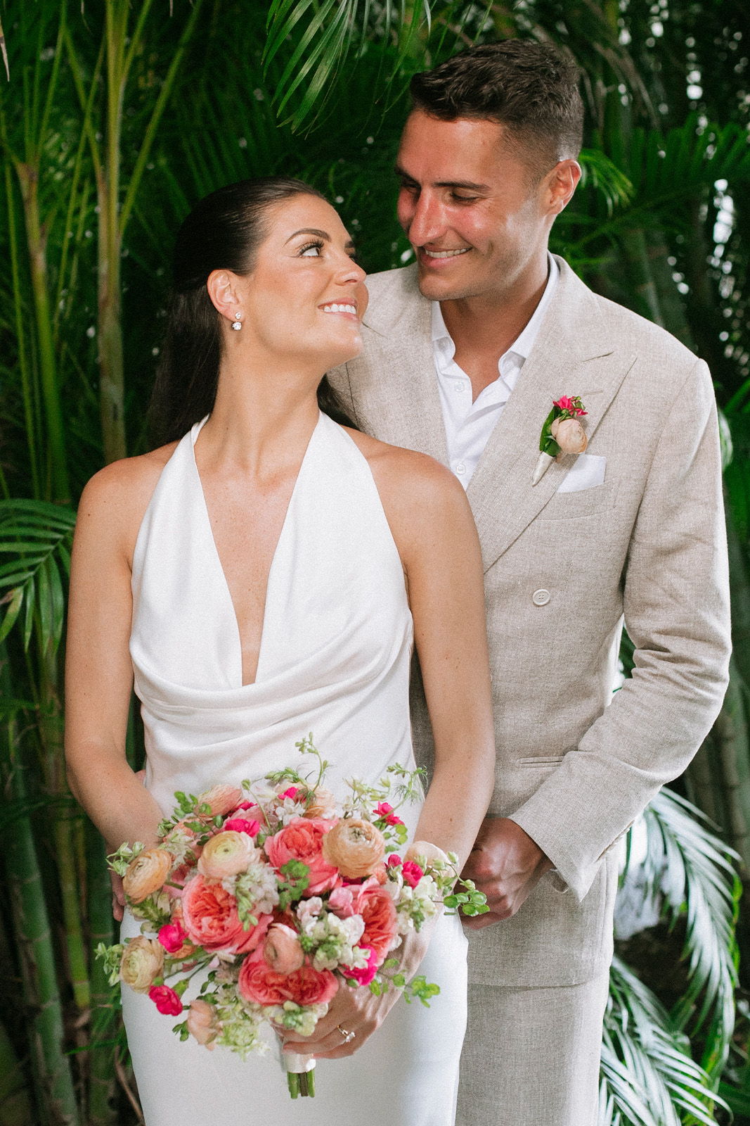 Bride and groom smiling together in a tropical setting with flowers.