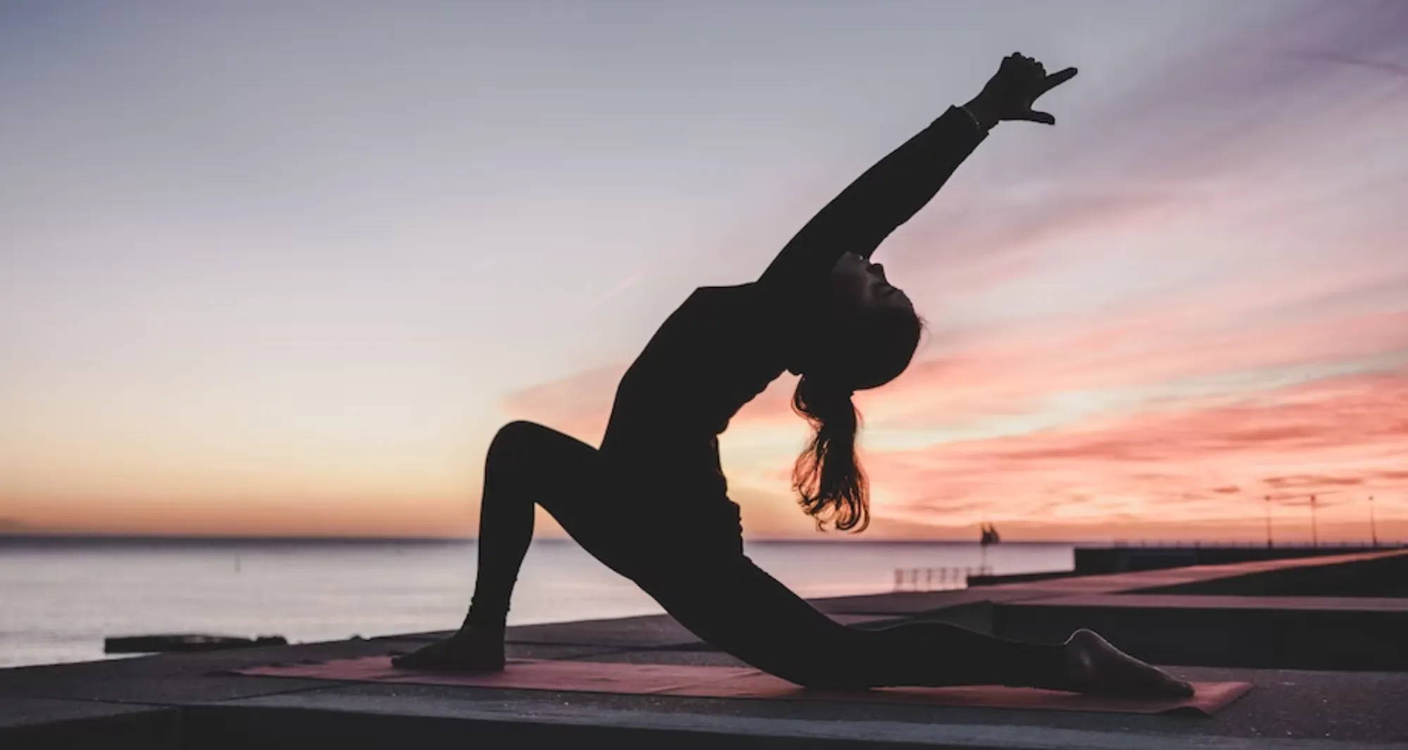 person doing a yoga pose on a dock at sunset