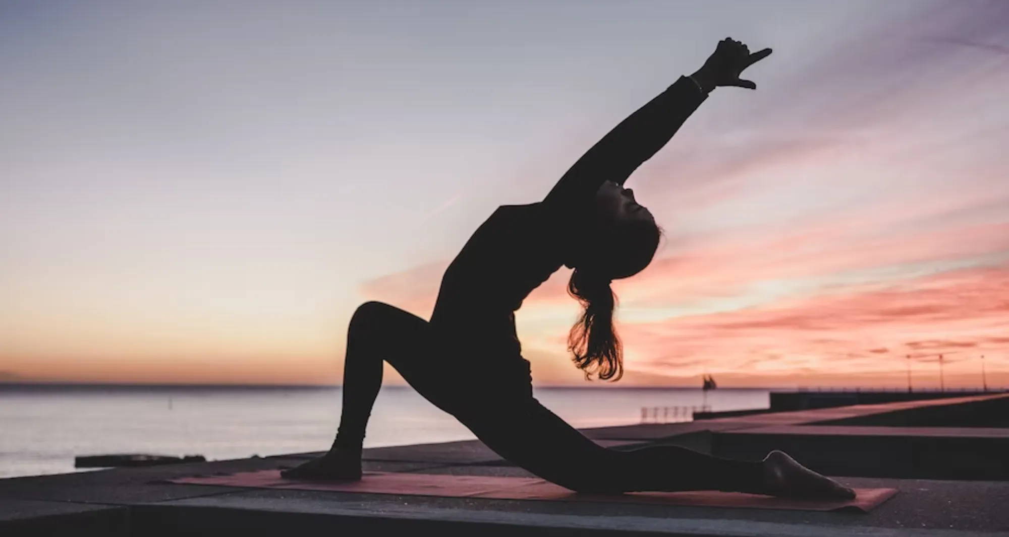 woman doing yoga at sunrise near the water