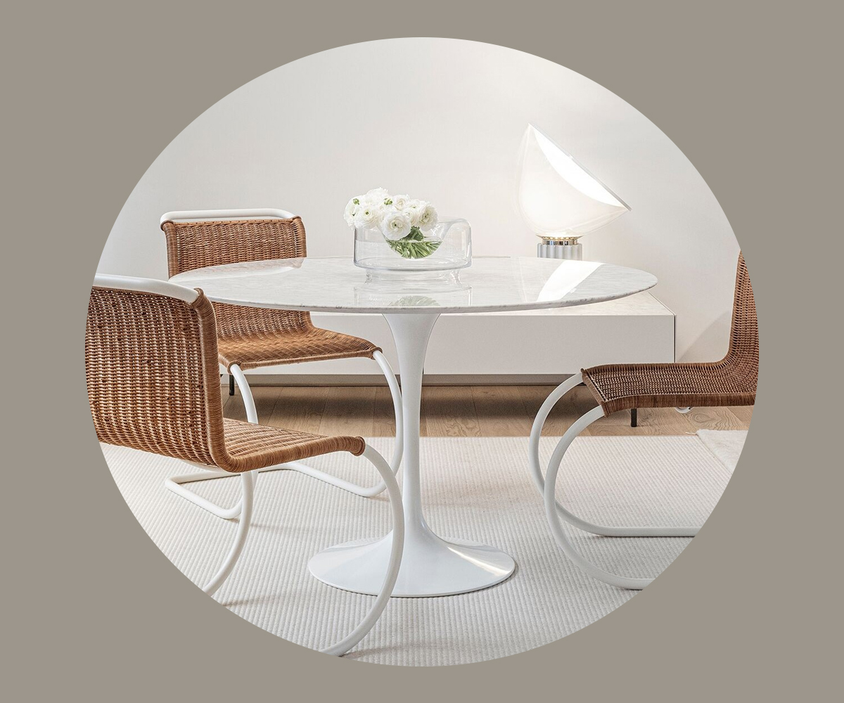 Modern Saarinen dining table with two rattan chairs and a vase of flowers.