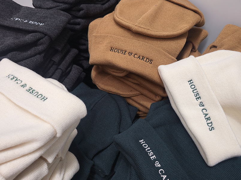 Stacks of green, grey, cream, and tan beanies embroidered with House of Cards logo on the cuff