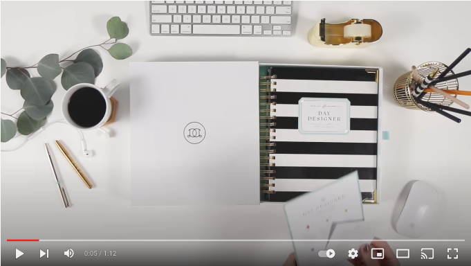 black and white stripped daily planner unveiling video, on white desk with pens, cup, tape dispenser, keyboard, computer mouse, coffee mug, ear buds