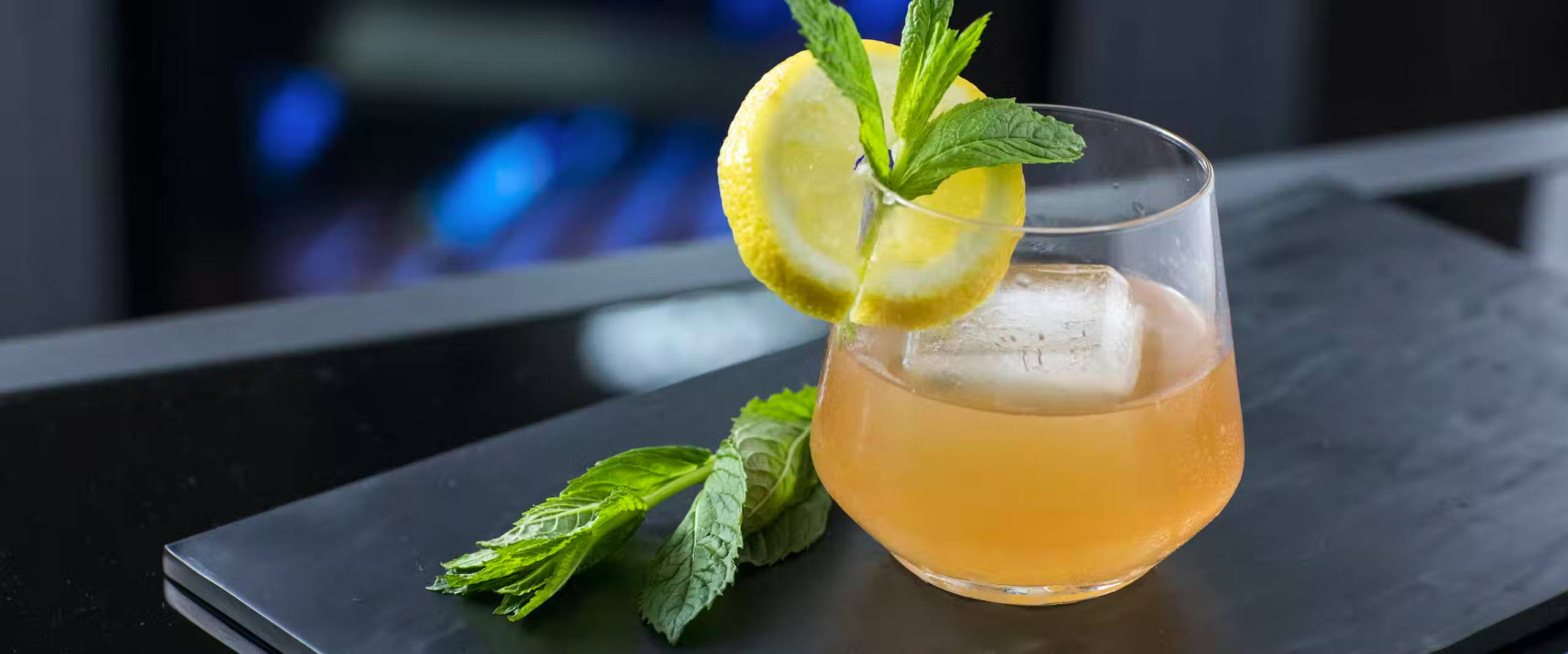 Close up of citrus bourbon cocktail in a glass with lemon and sprig of mint as garnishes