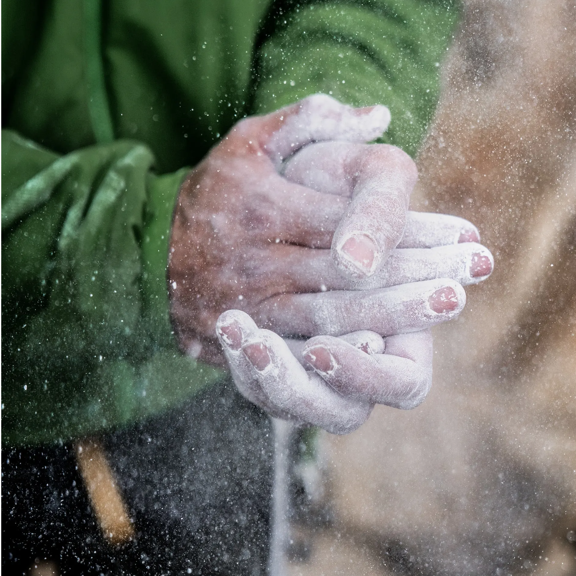 close up of a climber patting their hands in a cloud of chalk, probably psyching themselves up to get on the wall