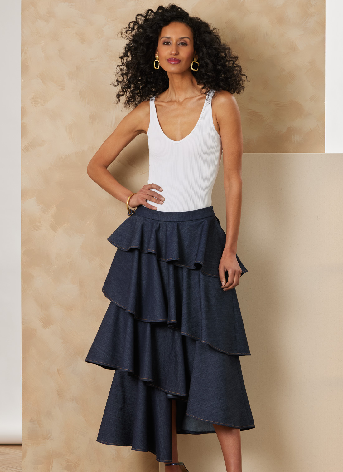 Woman in a white tank top and layered denim skirt against a neutral background.