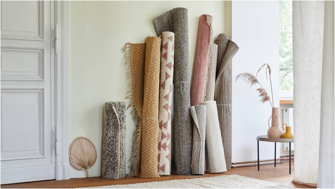 Various patterned and textured rugs leaning against a wall. A clean, minimalist space.