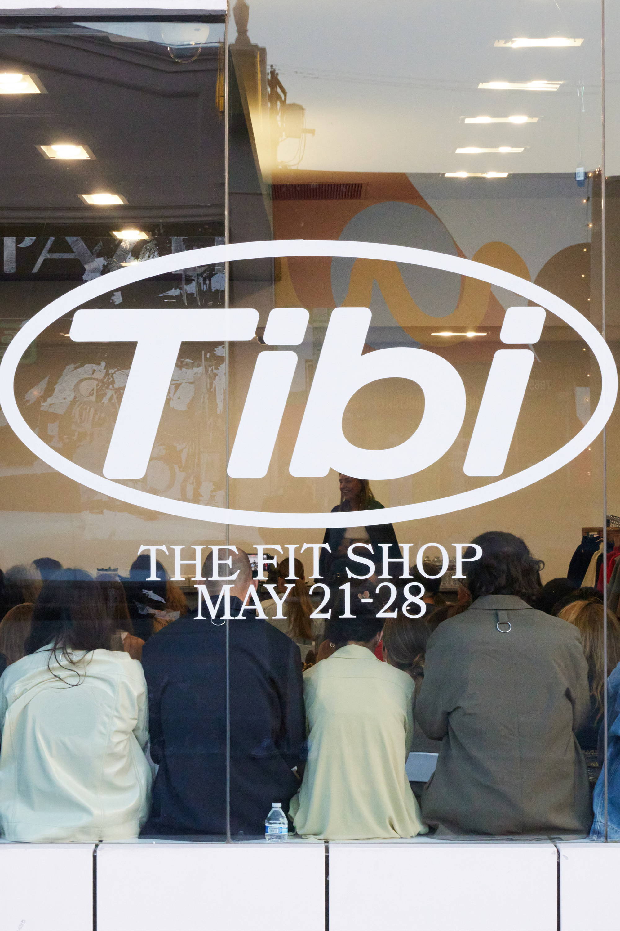 Group of people sitting behind a glass window with a store sign.
