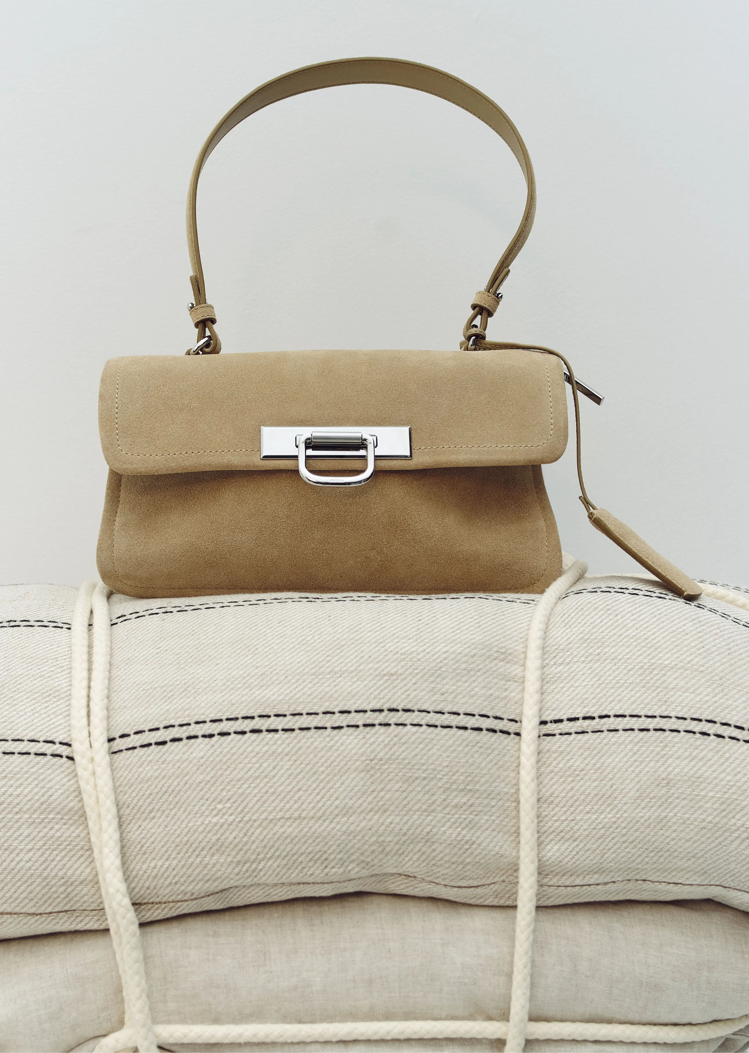 A beige handbag resting on a rolled-up fabric with rope detailing.