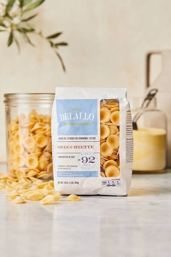 DeLallo Orecchiette pasta in its packaging in front of a jar filled with pasta.