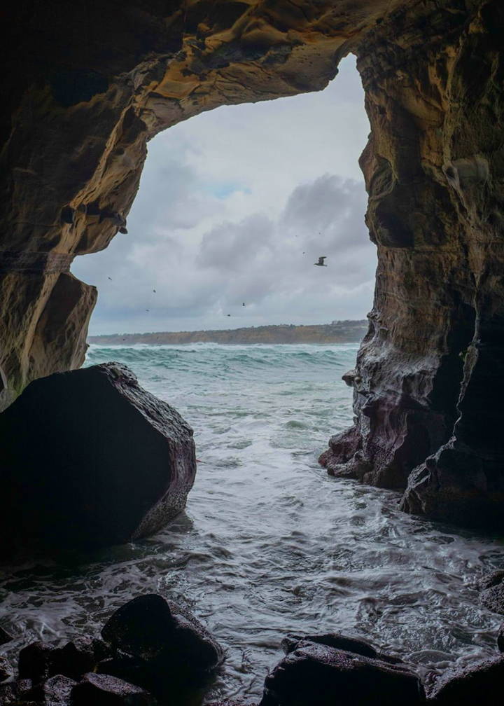 A photo from inside a sea cave, looking out towards the ocean. The lefthand and righthand side of the photo are framed by rock formations.