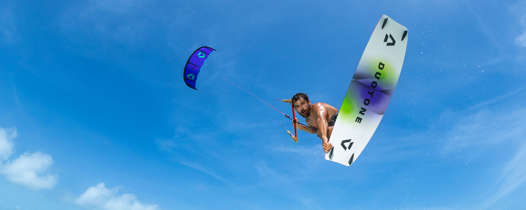 Une personne faisant du kitesurf dans le ciel, sur fond bleu.