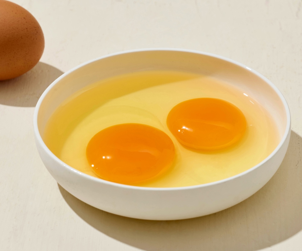 Two egg yolks in a white bowl, with an egg beside it.
