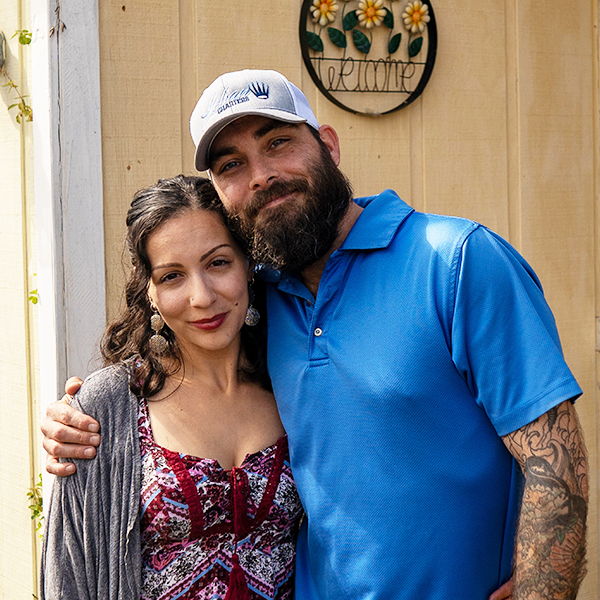 A couple posing together outdoors, smiling and embracing each other.