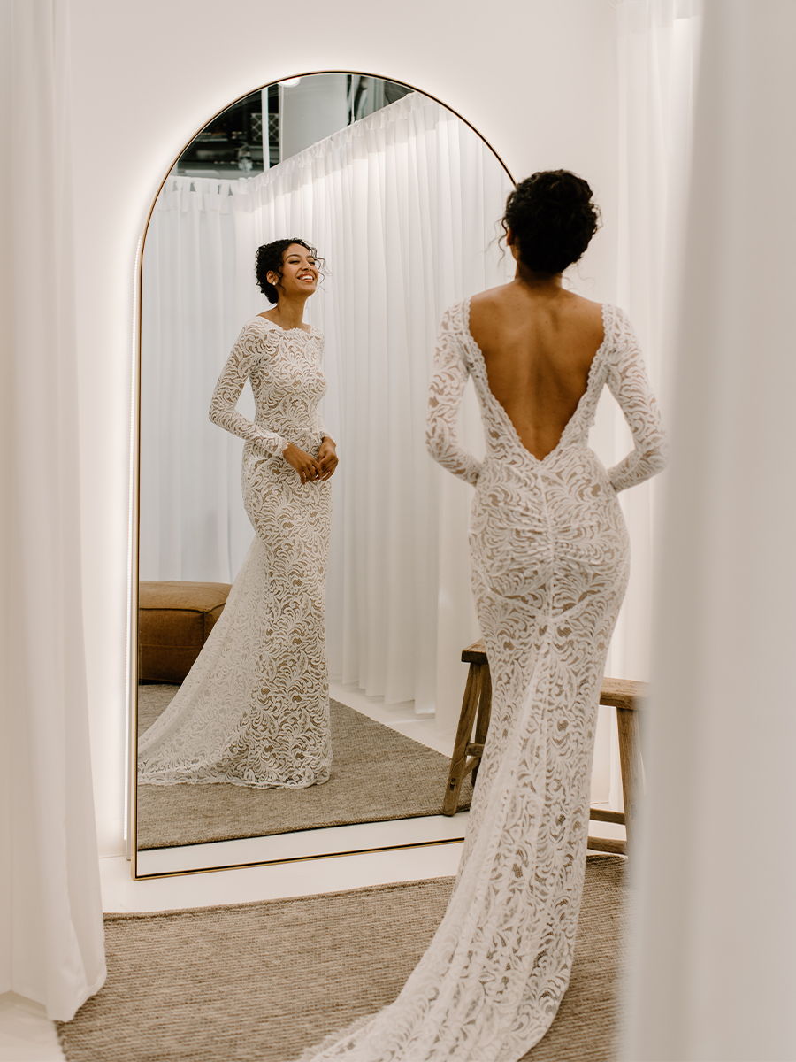 Woman in a lace gown admiring her reflection in a mirror.