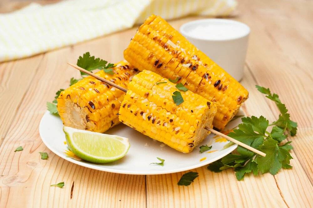 Barbecued corn on the cob on a plate with a slice of lime.