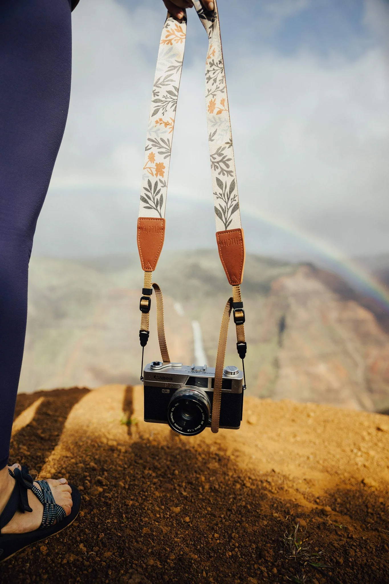 Wildflower camera strap in outside setting with rainbow.
