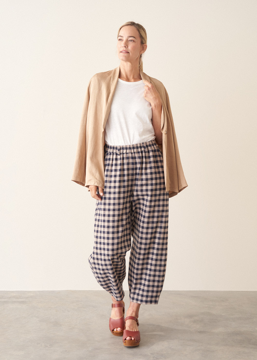 Woman wearing blue and taupe check barrel leg trousers with clog heels and a white t-shirt.
