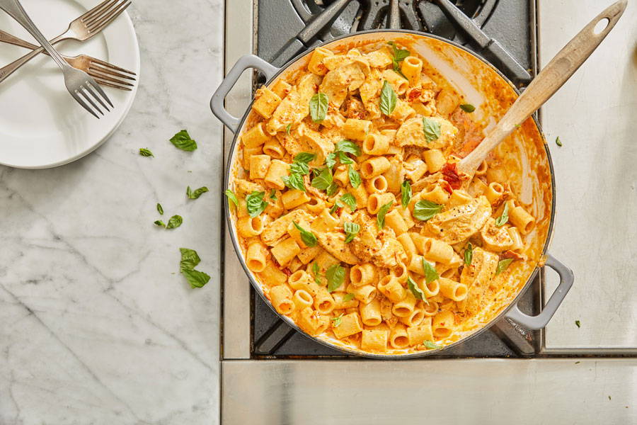 Rigatoni pasta in a creamy tomato and cheese sauce with chicken prepared in a pot topped with fresh basil leaves
