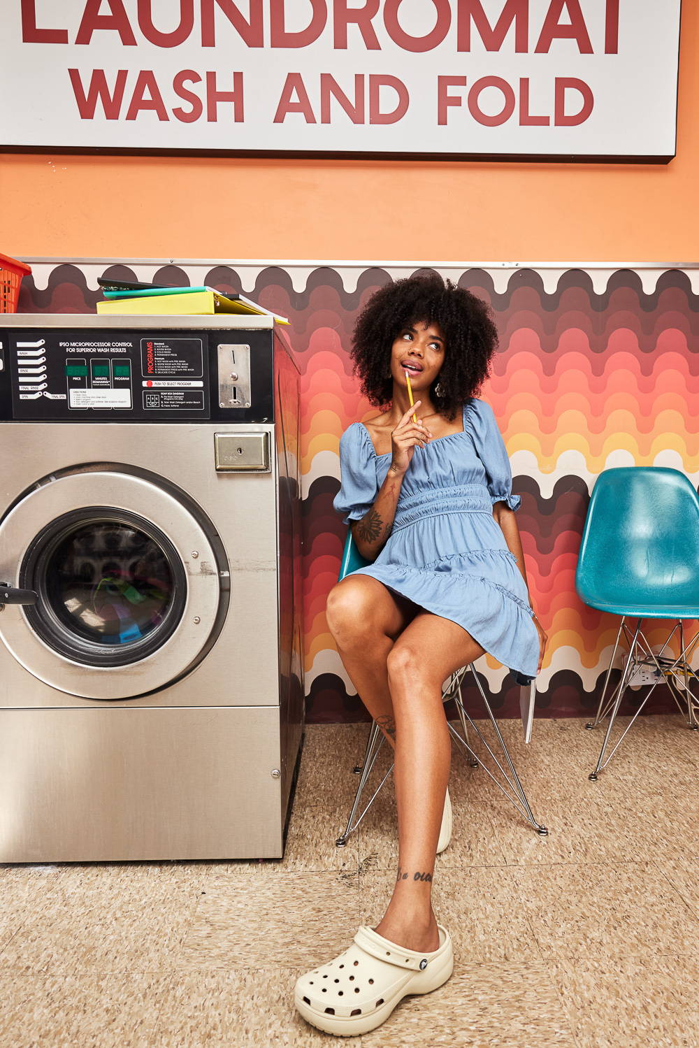Trixxi Back to school embracing dorm life doing laundry in a laundromat wearing a blue tier dress.