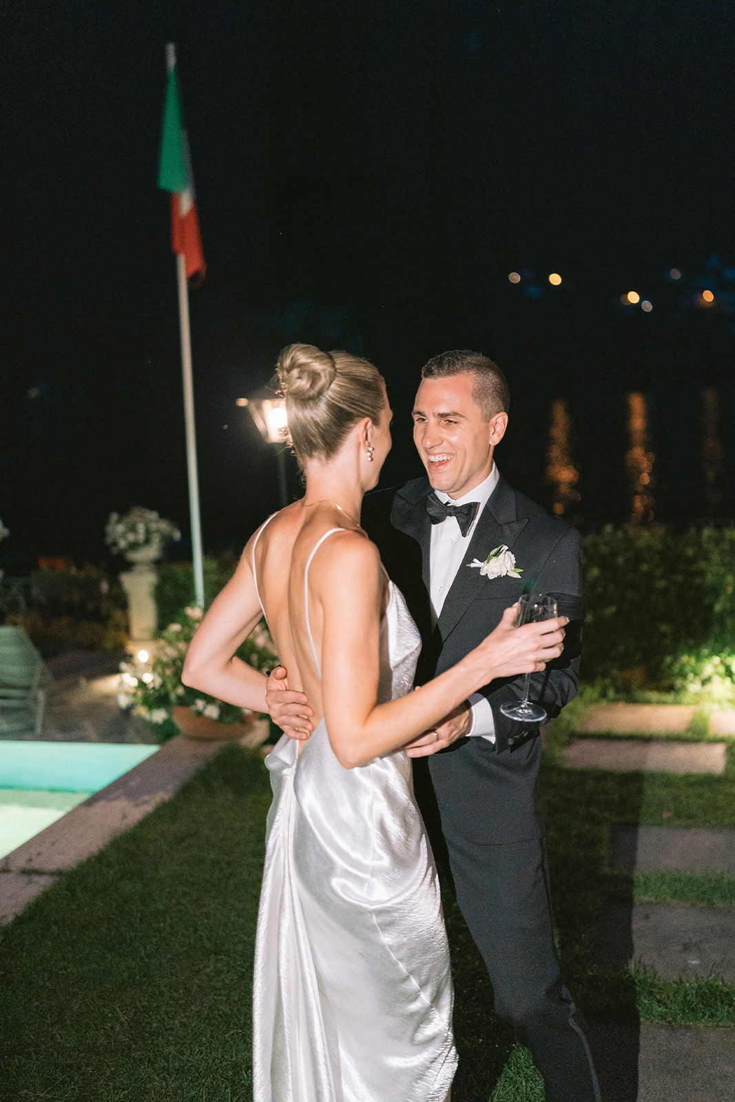 Couple dancing by a pool at night, with a flag in the background.