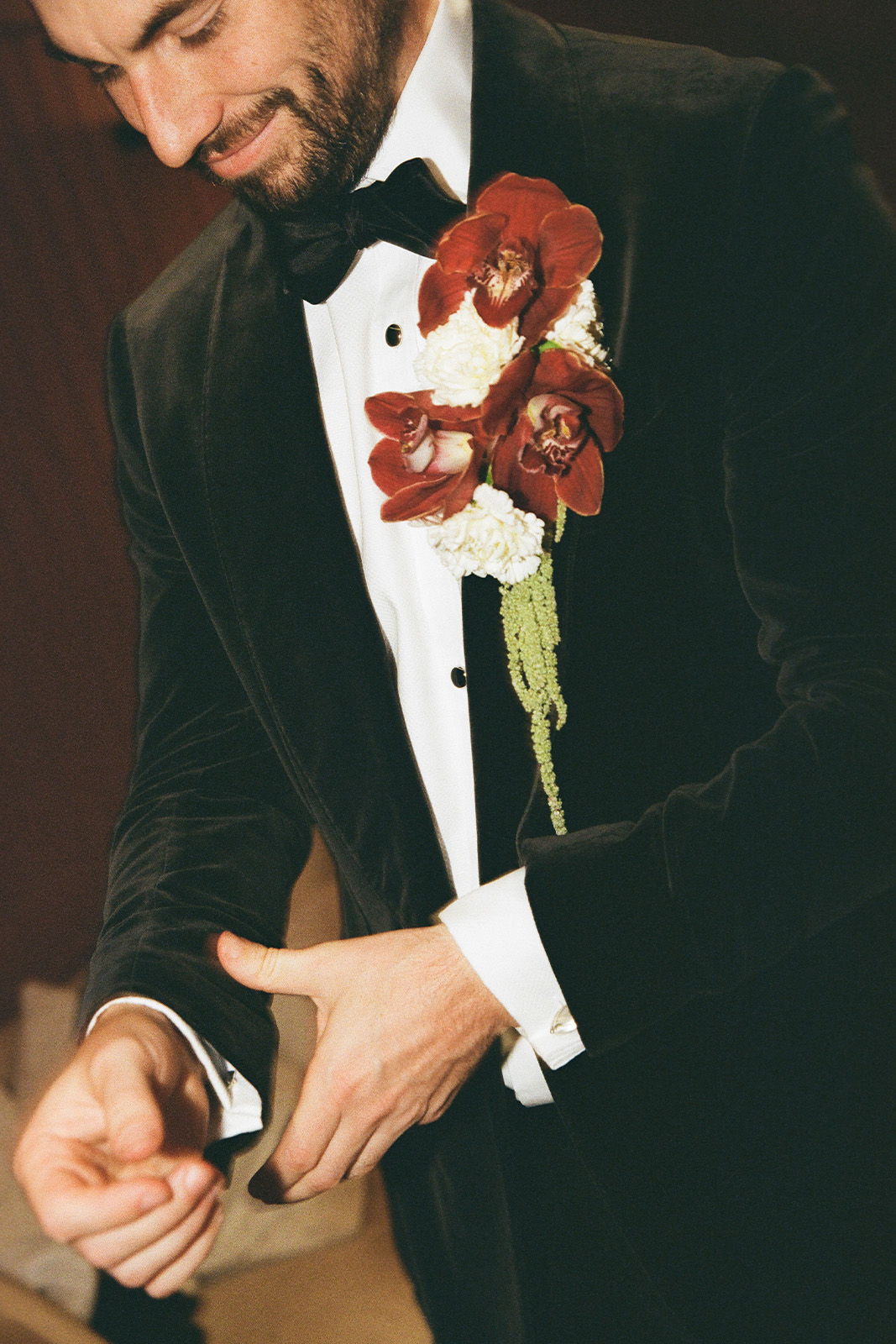 Man adjusting cufflinks, wearing a tuxedo with a floral boutonnière.