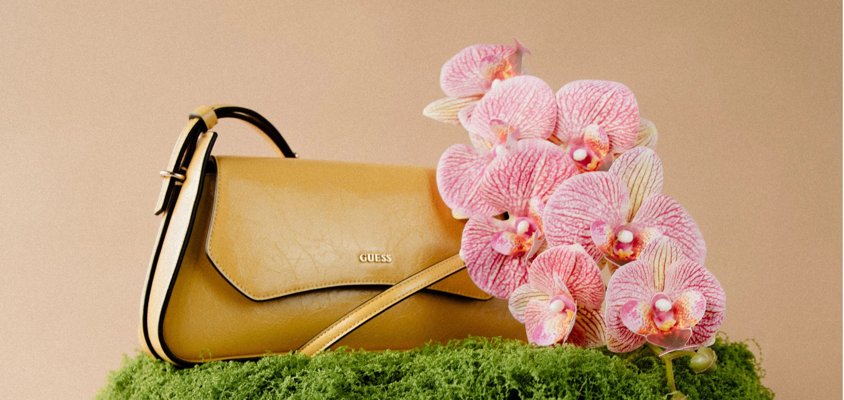 A yellow handbag with pink flowers on a mossy surface.