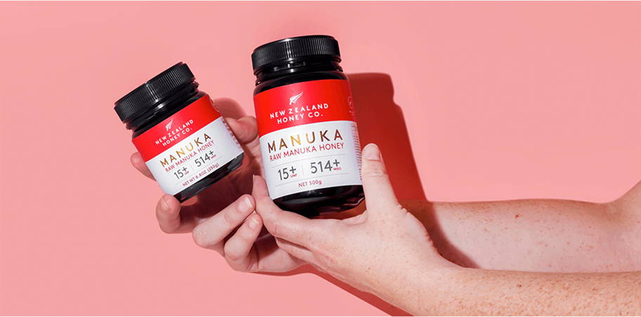 Two bottles of vitamins held in hands against a pink background.