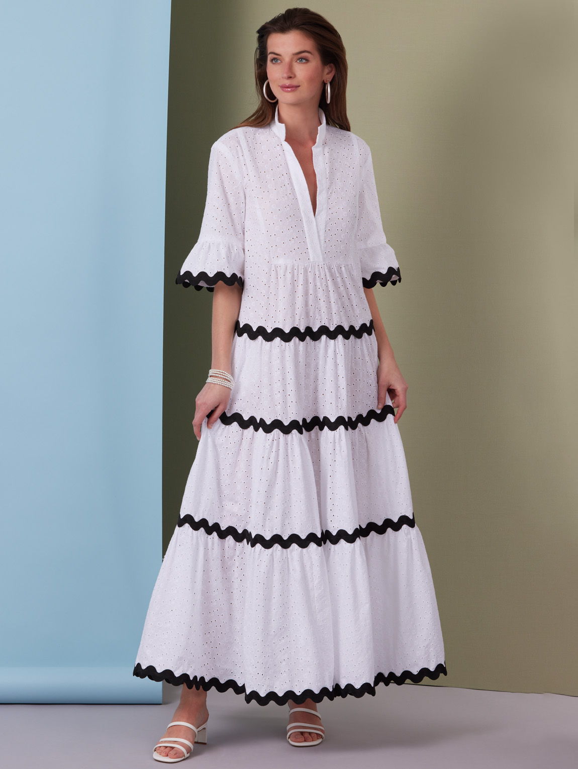 Model wearing a white dress with black trim against a pastel background.
