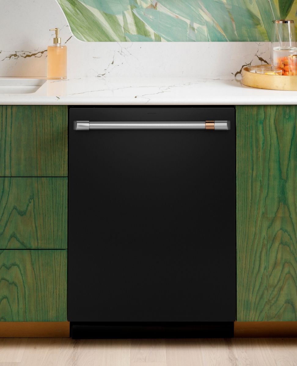 Black dishwasher under a countertop with green cabinets and decorative items.