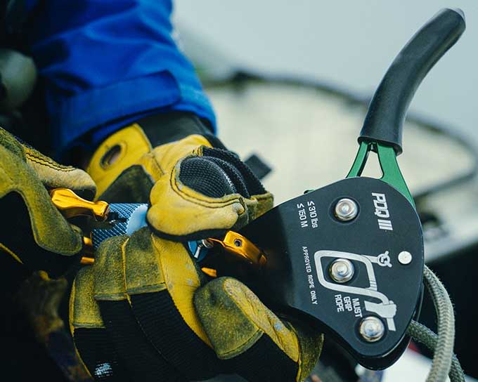 A close up view of person wearing gloves attaching carabiner to the PDQ3 emergency decent device.