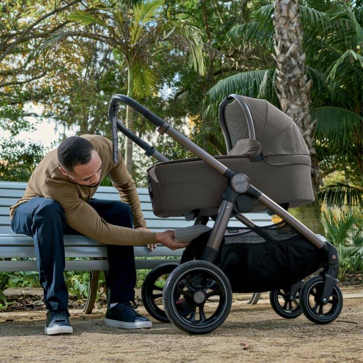 Man sat on a bench with a baby in an Ocarro pushchair