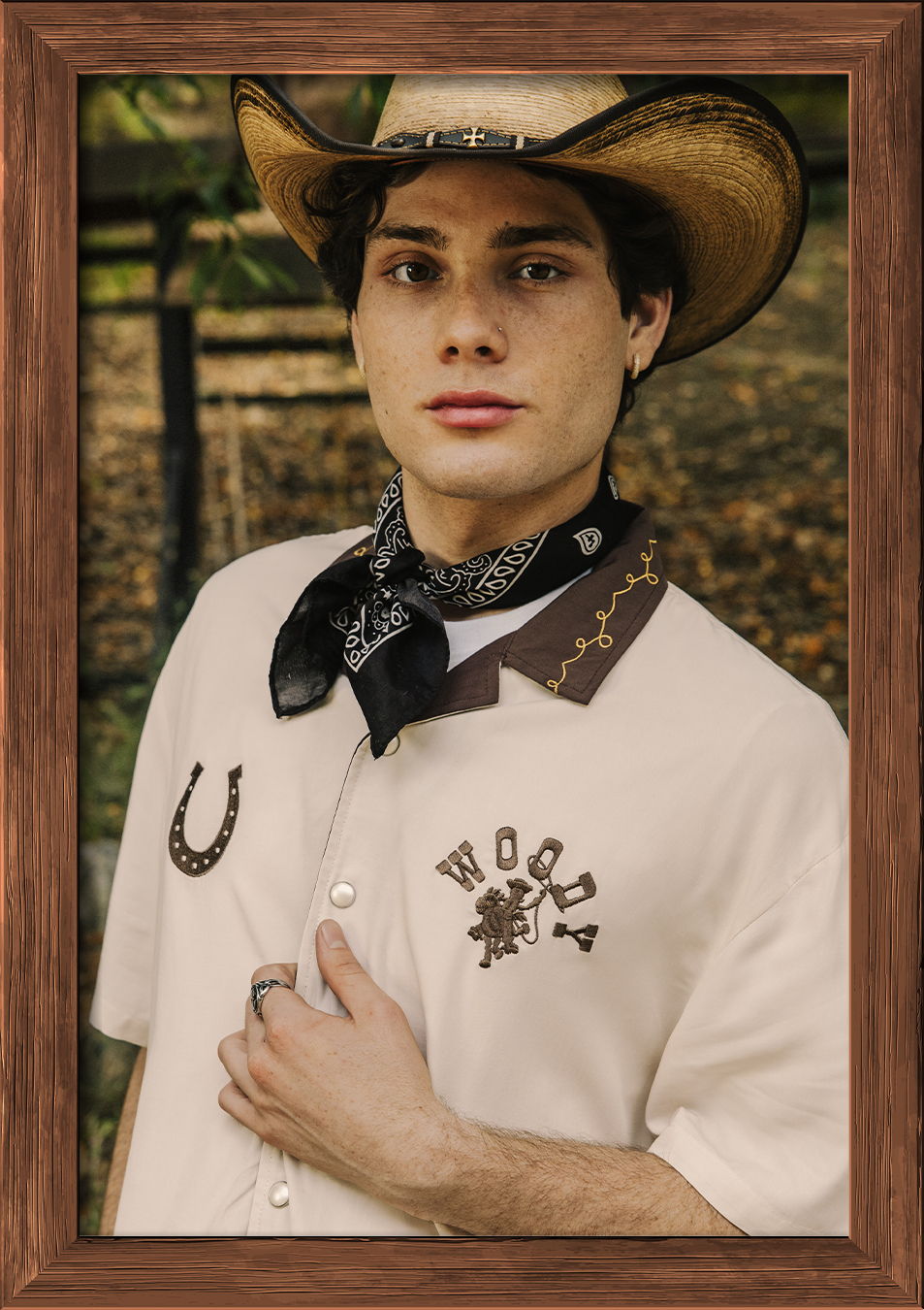 Young man in cowboy attire with hat and scarf, posing outdoors.