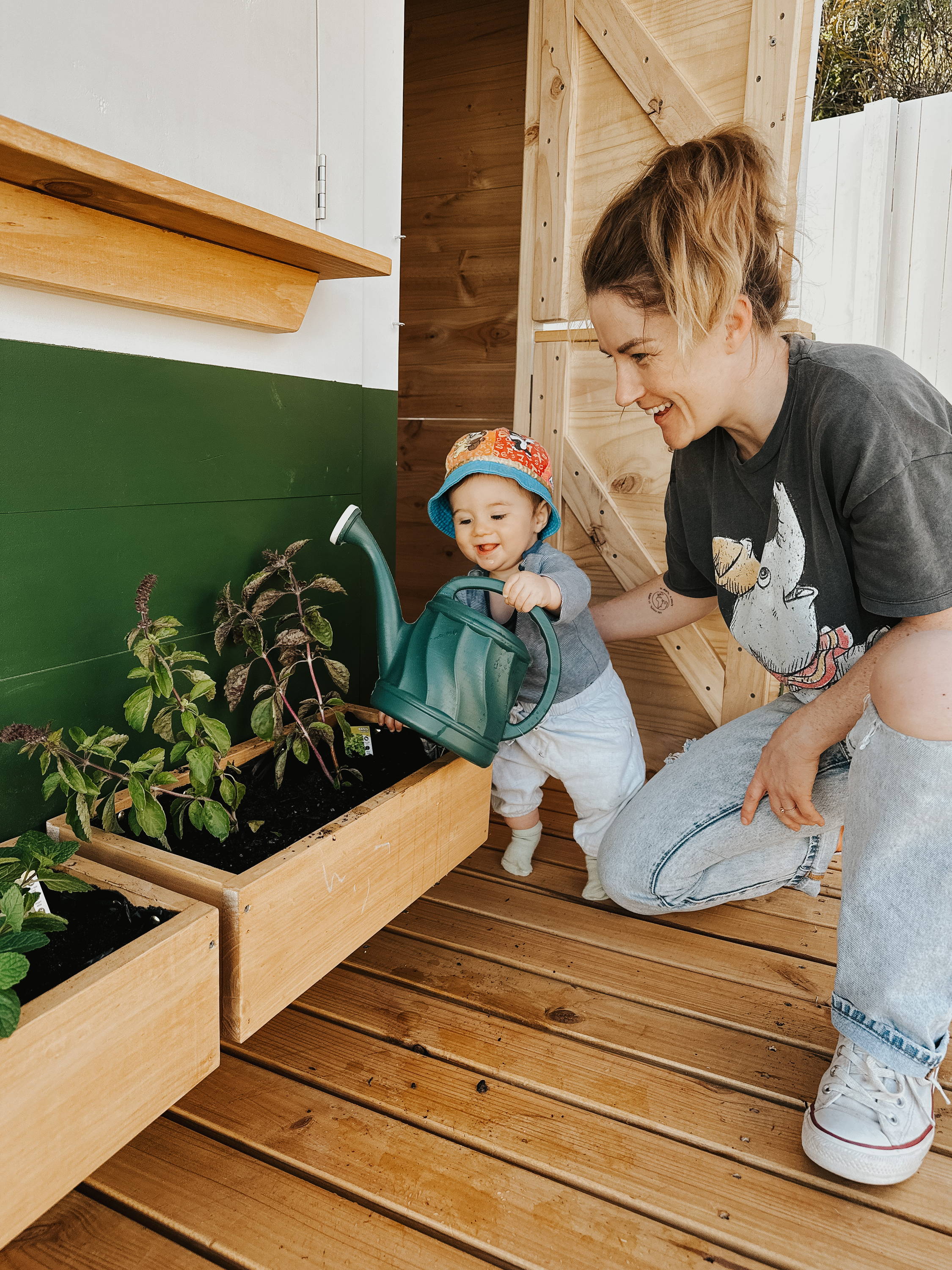 A mom and a kid watering a plant at one of cubby house's pots