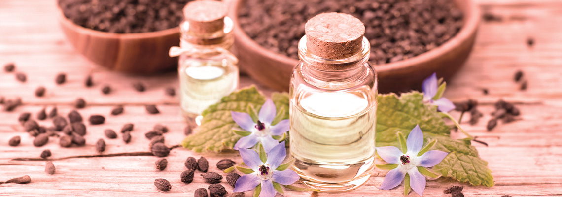 Bottles of essential oil with seeds and flowers in the background.