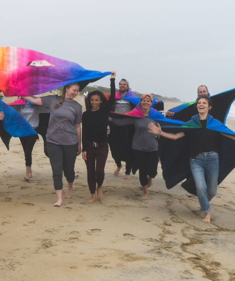 Members of First Descendants walk barefoot on a beach, wearing Rumpls as capes