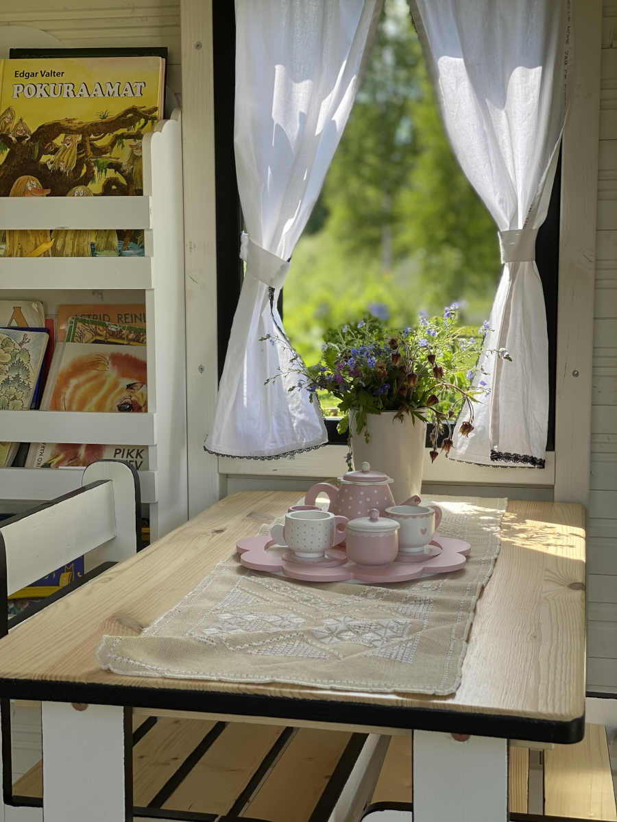 Closeup of window with curtains and kids table with kids tea set by WholeWoodPlayhouses