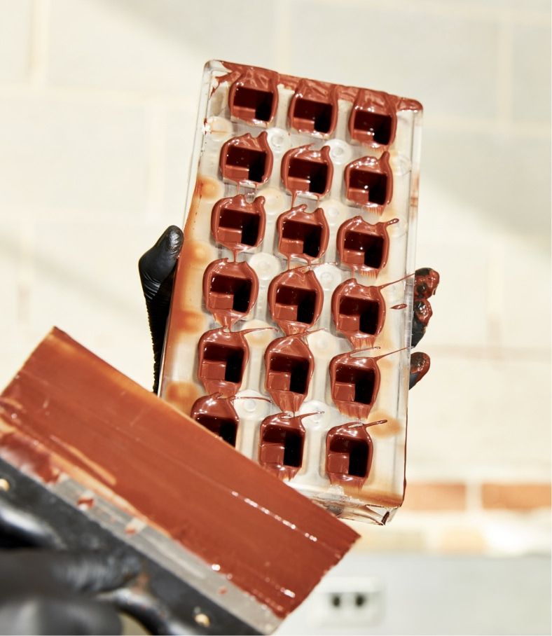 A person holding a chocolate mold filled with melted chocolate.